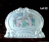 Front view of the white ceramic napkin holder with floral details and religious Precious Moments illustration showing four children and a dog at a table with inscription below.