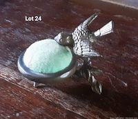 Photo of the antique tabletop brass pin cushion with a bird figurine on the side, showing the green velvet cushion with discoloration.