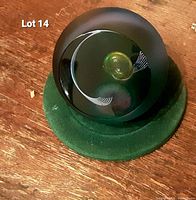 Front view of Caithness 'Star Conquest' glass paperweight showing central yellow orb and white curved lines inside clear to frosted glass sphere on green velvet base.