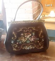 Front view of vintage petit point evening bag showing floral embroidery, leather sides, decorative metal top frame, and leather handle.