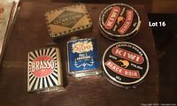 Photo showing five vintage tins including KIWI shoe polish tins, Brasso polish tin, Silvo polish tin, and Rowntree's Clear Gums tin on a wooden surface.
