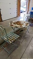 Full view of weathered metal folding bistro table and two matching chairs with heavy surface rust and peeling paint in garage.