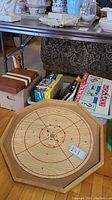 Wood Crokinole board prominently displayed with some board game boxes in background including Monopoly and Scrabble.
