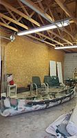 Full side view of 14-foot camouflage aluminum canoe inside garage showing overall condition and size relative to chairs nearby.