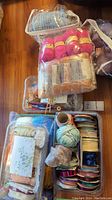 Overview of multiple containers holding yarn, ribbons, pipe cleaners, and lace trims in various colors