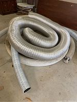 Coiled HVAC duct pipe and cloth-covered drainage pipe stacked together on concrete floor.