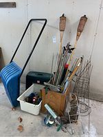 Full view of gardening and yard items grouped together showing shovel, step stool, wooden box with tools, stakes, cages, tiki torches, and garden ornaments.