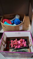 Two cardboard boxes, one holding pink and red dumbbells, the other holding blue and gray hand weights.