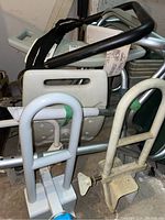 Photo showing white plastic backrest and several gray metal brackets and frames with some secured by green tape.