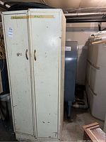 Front view of metal storage cabinet showing two doors with handles and wear marks on surface.