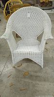 Front view of white painted wicker chair showing the fan-shaped backrest, armrests, seat, and paint chipping.