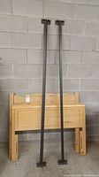 Wooden headboard, footboard and two tall metal rails leaning against a concrete block wall in a garage.