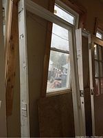 Two primed wood door frames leaning against a wall in a garage, one large and one smaller, visible window and plywood behind them.
