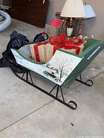Full view of the hand-painted vintage child's sleigh with decorative faux presents and attached candy cane lights, showing the metal frame and painted wooden side panels.