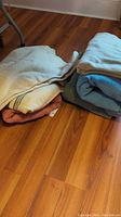 Photo showing two stacks of folded wool blankets on wooden floor, various colors visible