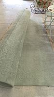 Rug partially rolled out on concrete floor showing embossed pattern and pile thickness