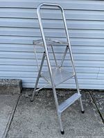 Side view of aluminum ladder against siding showing two steps, small platform, handle and rubber feet.
