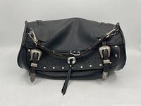 Front view showing the entire black leather bag with two large decorative silver buckles and studs along the flap.