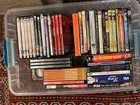 Plastic container filled with various DVD sets organized by type and title visible.
