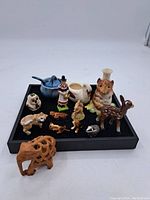 Lot of assorted small figurines including animals and miniature pottery displayed on black tray.
