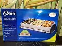 Photo shows the original box of the Oster Triple Buffet Server with product image and feature highlights.