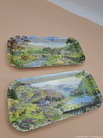 Both trays laid flat on a beige surface showing their detailed scenic prints