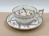 Angle view of Royal Chelsea porcelain tea cup and saucer showing decorative floral pattern with gold highlights and blue rim detail.