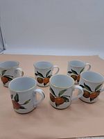Set of six Royal Worcester Evesham mugs arranged side by side, showing the fruit and leaf pattern with gold-rimmed edges.