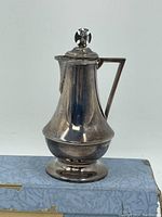 Full view of the sterling silver mini pitcher showing its shape, handle, lid with finial, and base profile.