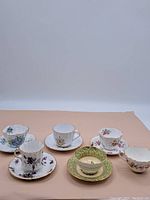 Front view of six vintage tea cups and matching saucers on a neutral background showing various floral patterns and gold trim.