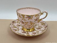 Tea cup and saucer set showing floral patterns and gold accents on white base.