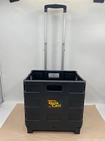Front view of the black plastic ultracompact Quik Cart with extended handle showing the logo on the side.