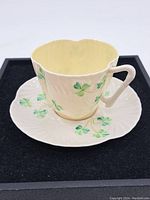 Side view of the Belleek Irish tea cup resting on the matching saucer, showing green shamrock decoration and scalloped cup rim.