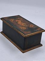 Rectangular black wooden box with gold and red decorative edges and central religious painting on lid showing a praying woman in profile.