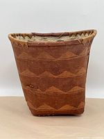 Front view of basket showing natural brown color, textured surface and horizontal rows of triangular geometric pattern in lighter brown.