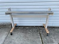 Front view of vintage wheeled stand with two metal rollers and white metal frame with wooden base and caster wheels.