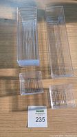 Stacked clear plastic drawer organizer trays arranged on table, shows rectangular and square shapes.