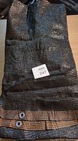 Folded black shade cloth with grommets visible on reinforced edge and numbered lot tag placed on top.