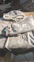 Grey oversized sherpa fleece blanket hoodie folded on table showing front kangaroo pocket and hood with sherpa fleece lining.