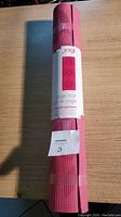Photo of a rolled pink Jogi yoga mat with patterned surface and attached white label showing brand and product details.