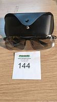 Men's wraparound photochromic polarized sunglasses displayed with black textured protective case and auction lot number.