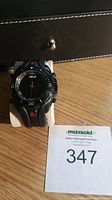 Black Timex Ironman Triathlon watch displayed on a padded stand with seller lot number card beside it, showing watch face and strap details.