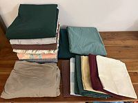 Stack of variously colored bedding including dark green, floral, and geometric patterned duvet covers, stacked on table.