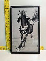 Front view of framed Asian ink painting of a running horse with ruler for scale.