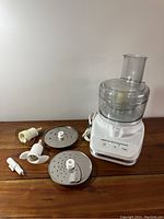 KitchenAid food processor with various attachments including discs and dough hooks arranged on a wooden table.