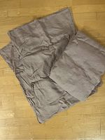 Photo of folded beige/taupe linen duvet cover and pillowcases on wood floor