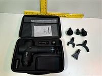 Full view of Abox massage gun, charger, six massage heads, and carrying case with mesh pocket and instruction manual inside. Includes measuring ruler for size reference.