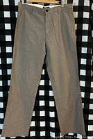 Front view of new Banana Republic men's dress pants, size 33x32, showing front zipper, button closure and belt loops, hanging against a black and white check background.