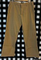Front view of new Banana Republic men's khaki pants, size 33x30, hanging on hanger with black and white checkered background
