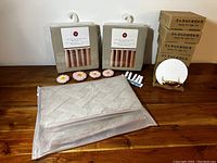 Includes two packaged beige linen and cotton shower curtains, hair dryer holders, floral candles, clothes pins, small round mirror, and bath mats in packaging.